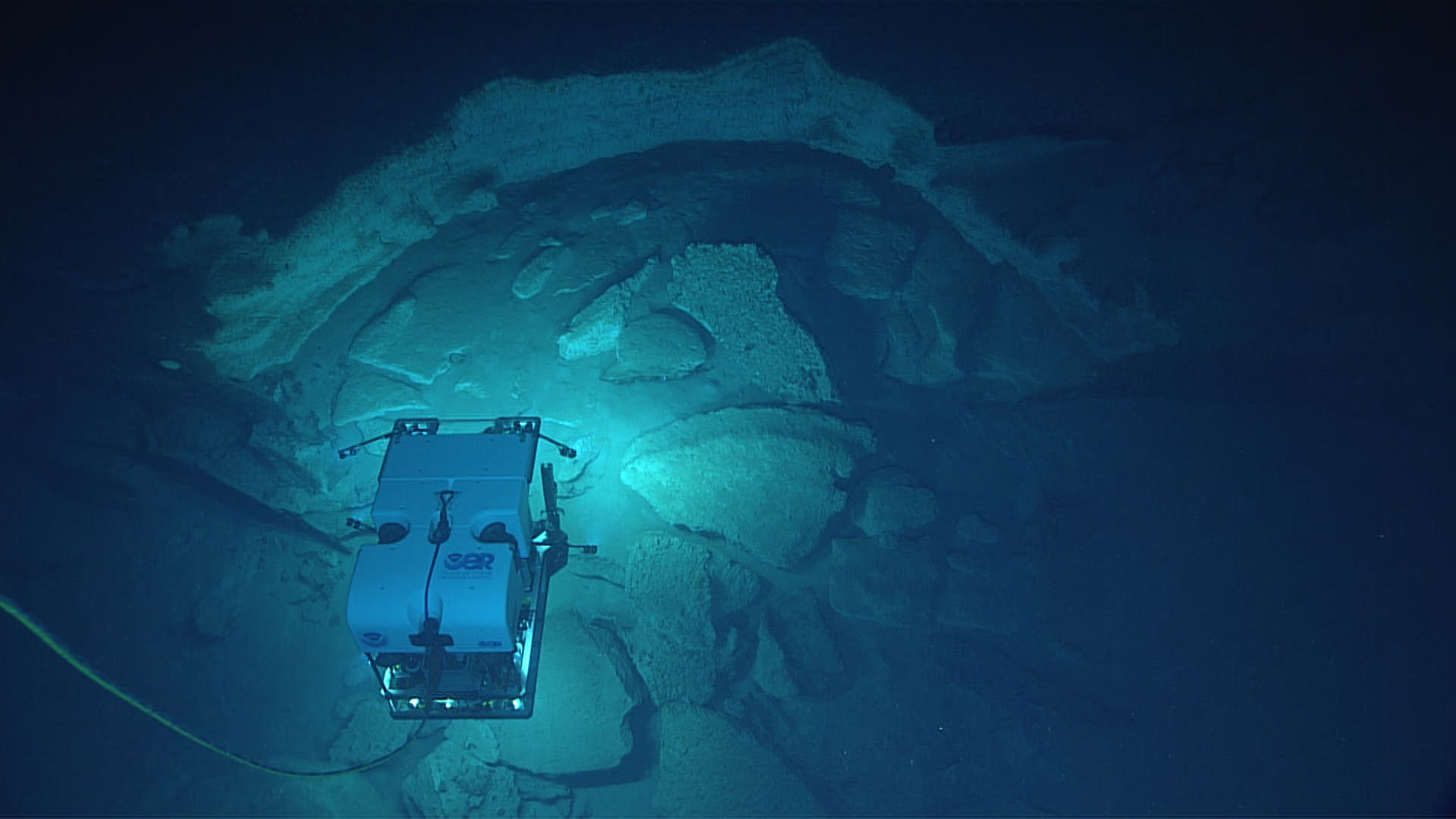 Figure 2. Remotely operated vehicle Deep Discoverer investigates some of the striking geology seen at “Okeanos Ridge” during Dive 03 of the Gulf of Mexico 2017 expedition. Image courtesy of NOAA’s Office of Ocean Exploration and Research. Download larger version (jpg, 359 KB).